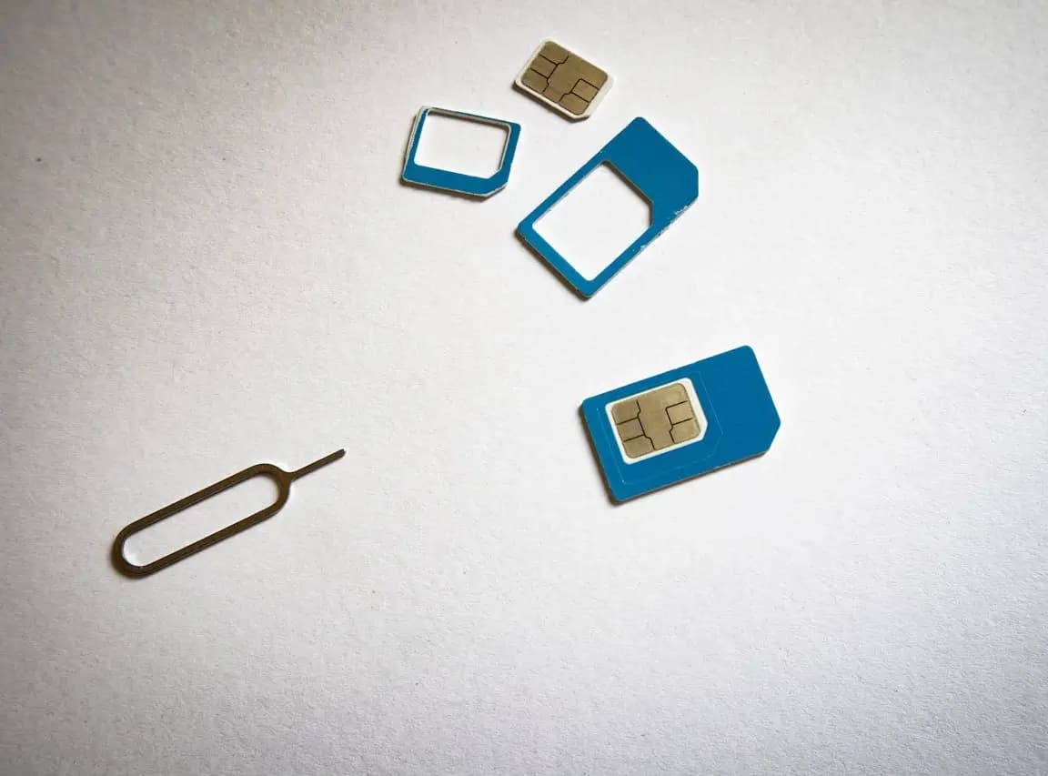 Różne rozmiary kart SIM i narzędzie do tacki SIM leżące na jasnym tle. Ilustracja problemu z niewykrywaną kartą SIM w telefonie.