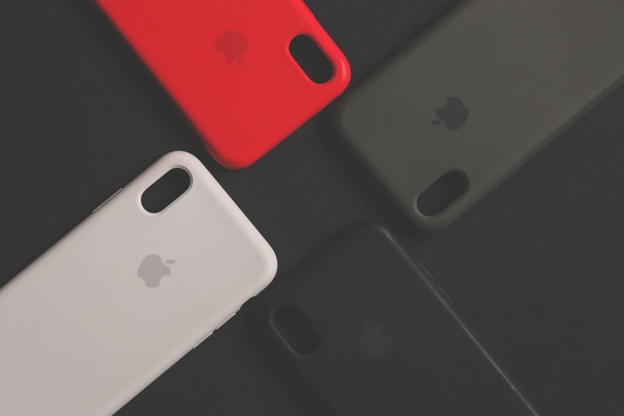 Oryginalne etui Apple w trzech kolorach - czerwonym, białym i czarnym - na ciemnym tle, prezentujące różne opcje zabezpieczenia iPhone'a wysokiej jakości pokrowcami