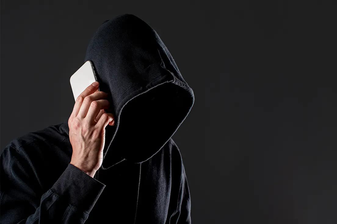 Zakapturzona postać z telefonem przy uchu symbolizująca potencjalnego złodzieja telefonów
