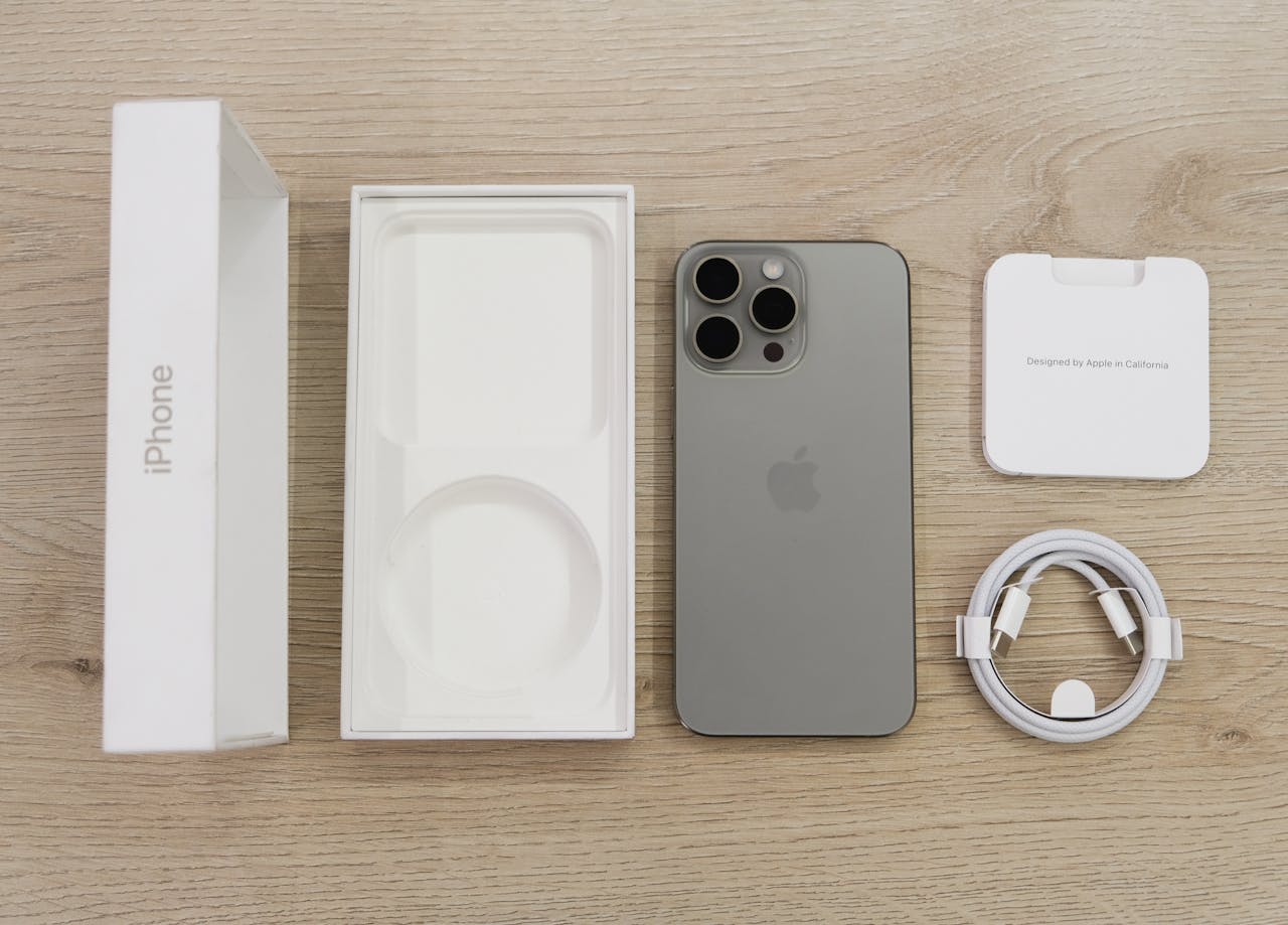Używany iPhone 13 Pro w kolorze grafitowym z kompletnym zestawem: oryginalne pudełko, wkładka, kabel USB-C i dokumentacja na drewnianym blacie.