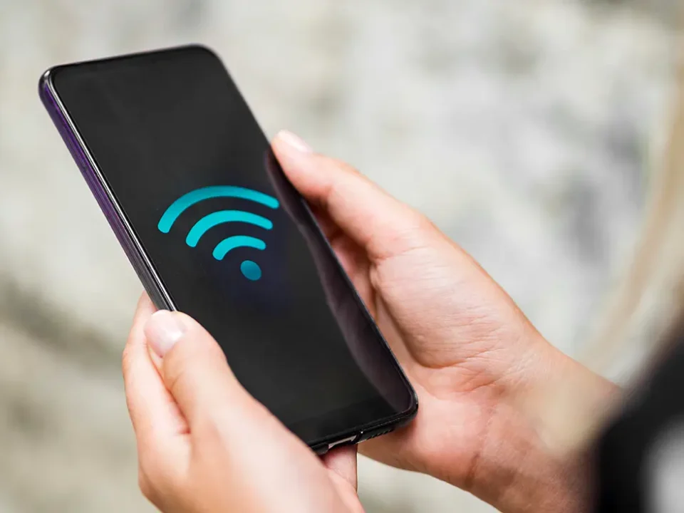 Osoba trzyma w dłoniach smartfon z wyświetlonym niebieskim symbolem WiFi na czarnym ekranie.