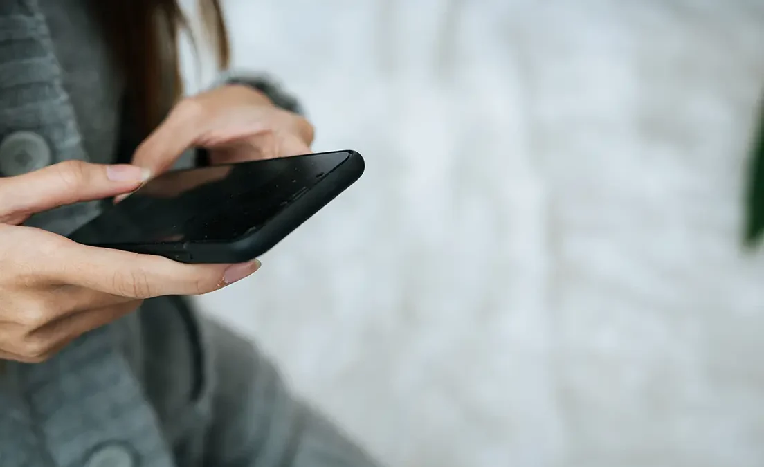 Kobieta trzyma w dłoniach smartfon z całkowicie czarnym, niedziałającym ekranem.