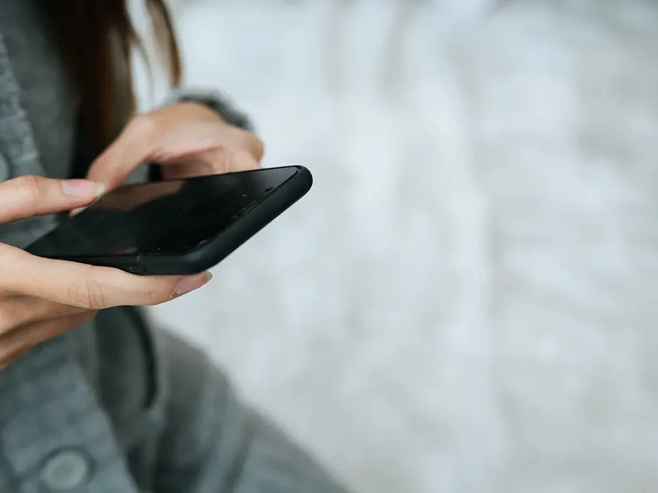 Kobieta trzyma w dłoniach smartfon z całkowicie czarnym, niedziałającym ekranem.