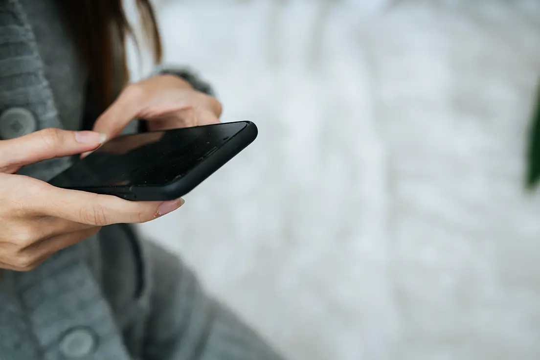 Kobieta trzyma w dłoniach smartfon z całkowicie czarnym, niedziałającym ekranem.
