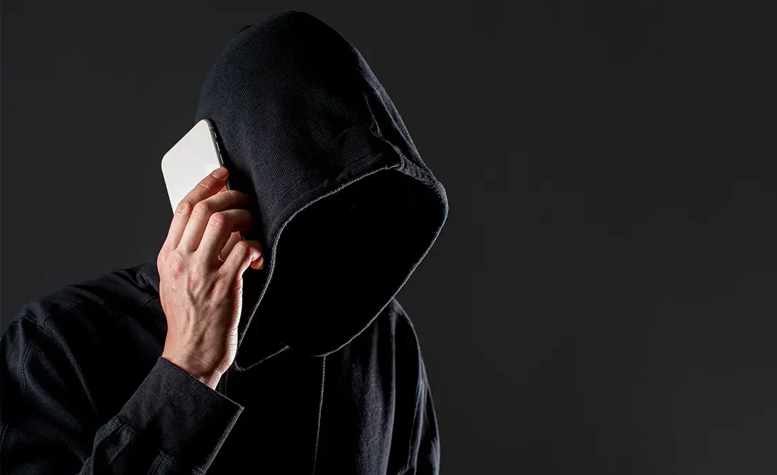 Zakapturzona postać z telefonem przy uchu symbolizująca potencjalnego złodzieja telefonów