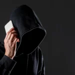 Zakapturzona postać z telefonem przy uchu symbolizująca potencjalnego złodzieja telefonów