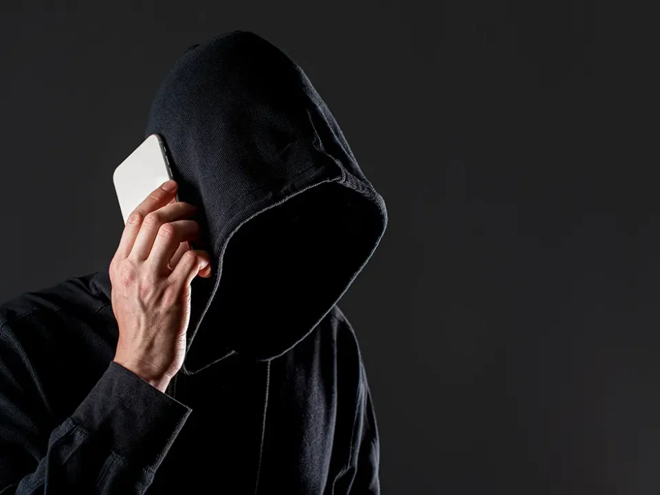 Zakapturzona postać z telefonem przy uchu symbolizująca potencjalnego złodzieja telefonów